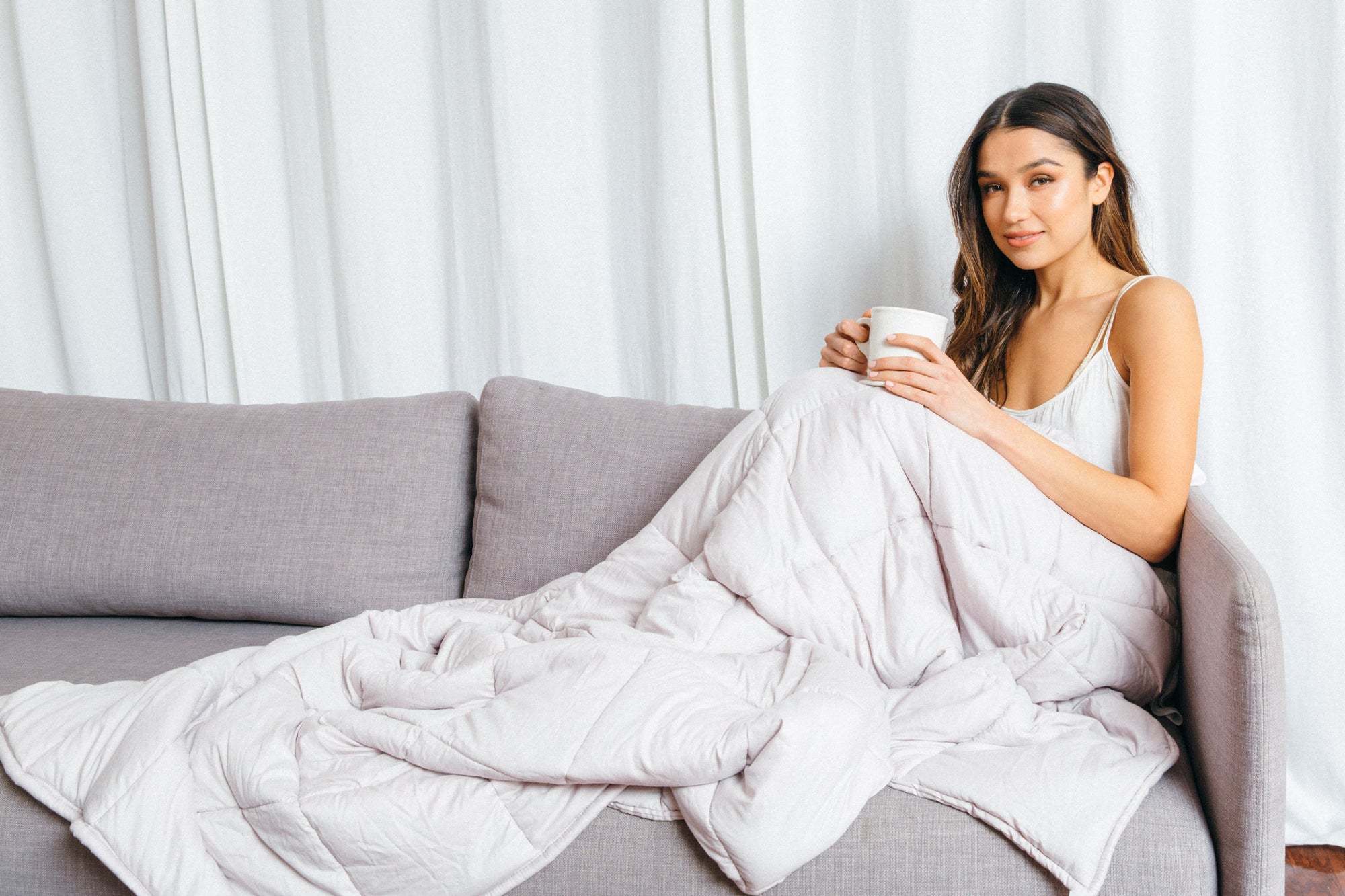 woman under weighted blanket with coffee