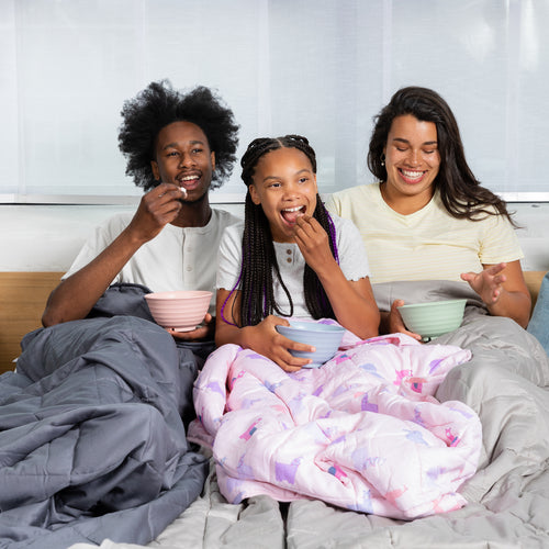 mom dad and daughter in bed eating popcorn